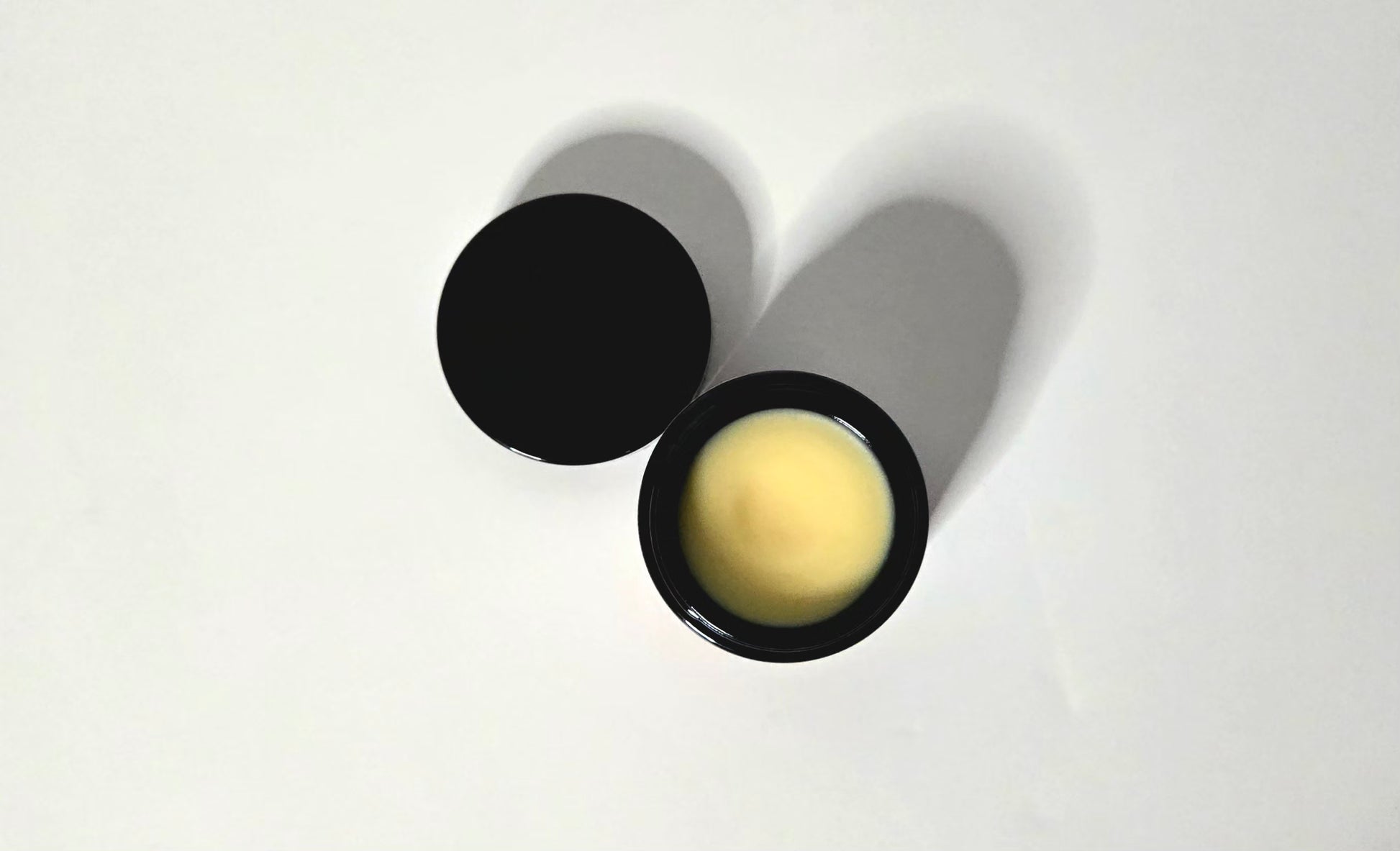 Black body butter container with a white balm inside on a white background