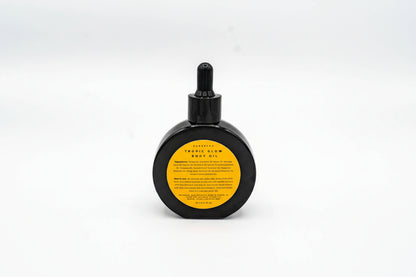 Black bottle of Tropic Glow body oil with a yellow label on a white background