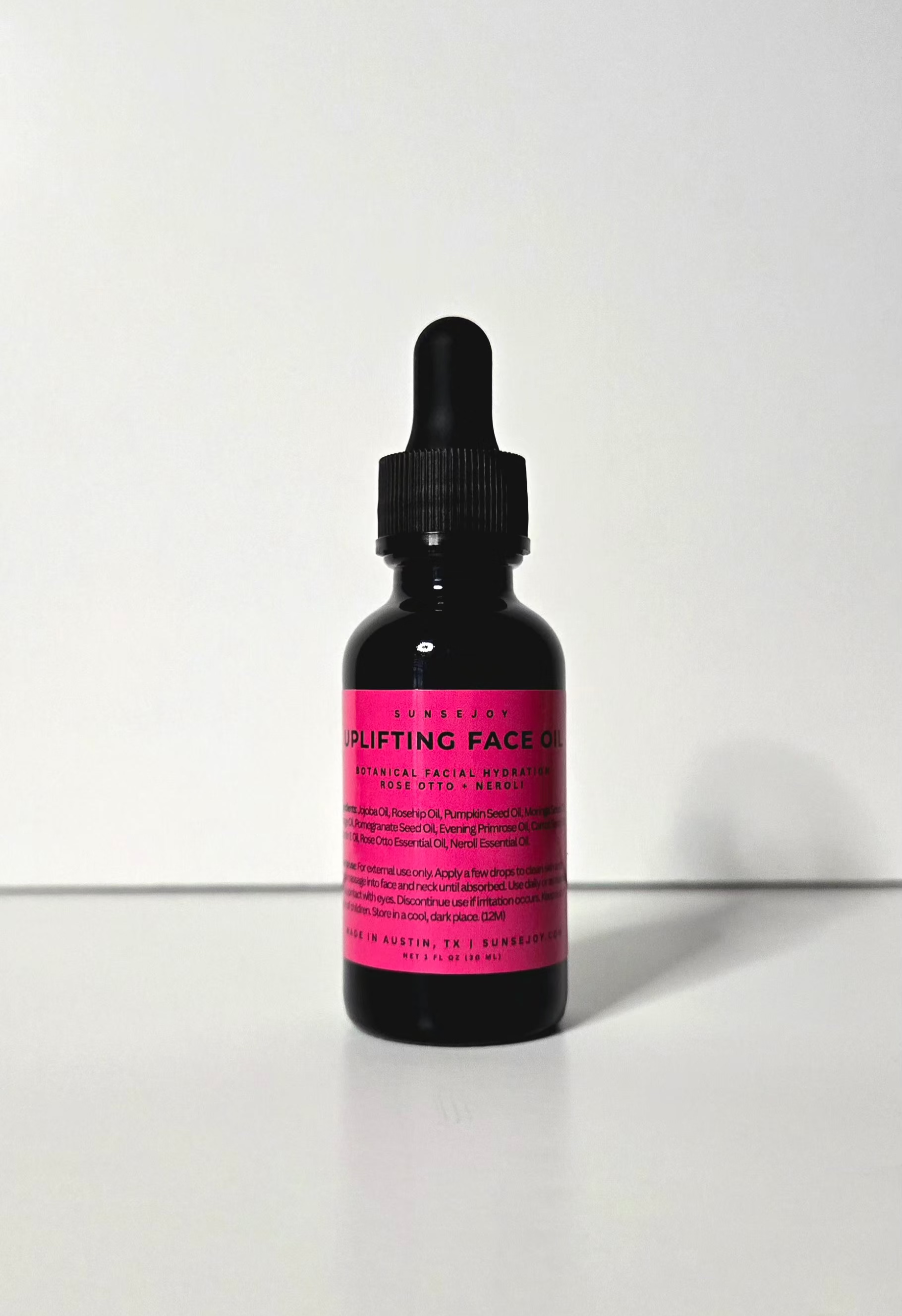Bottle of 'uplifting face oil' with pink label on a white background
